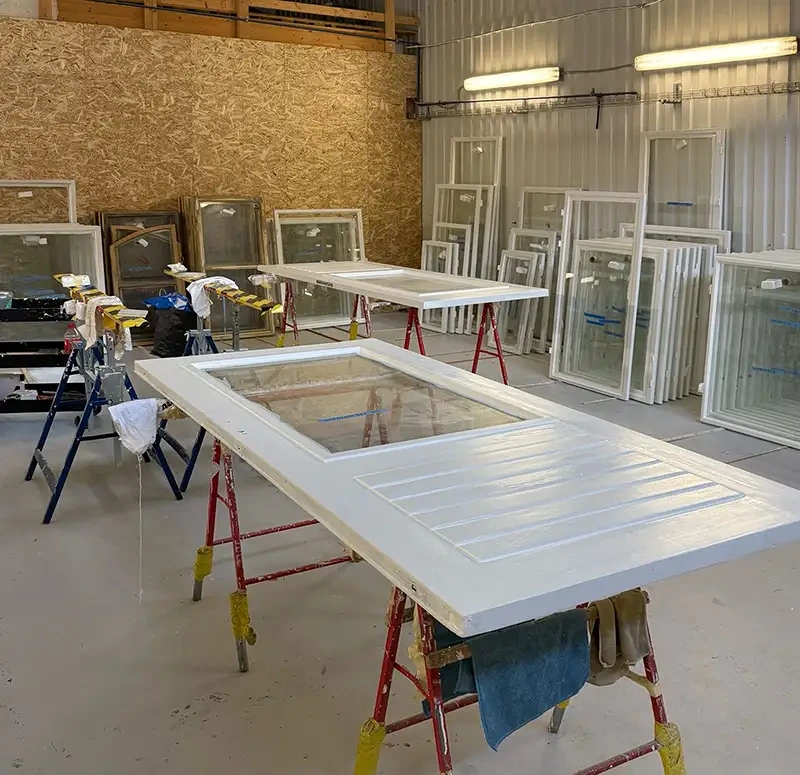 Verkstad med vita dörrar och fönster under renovering på arbetsbockar.
