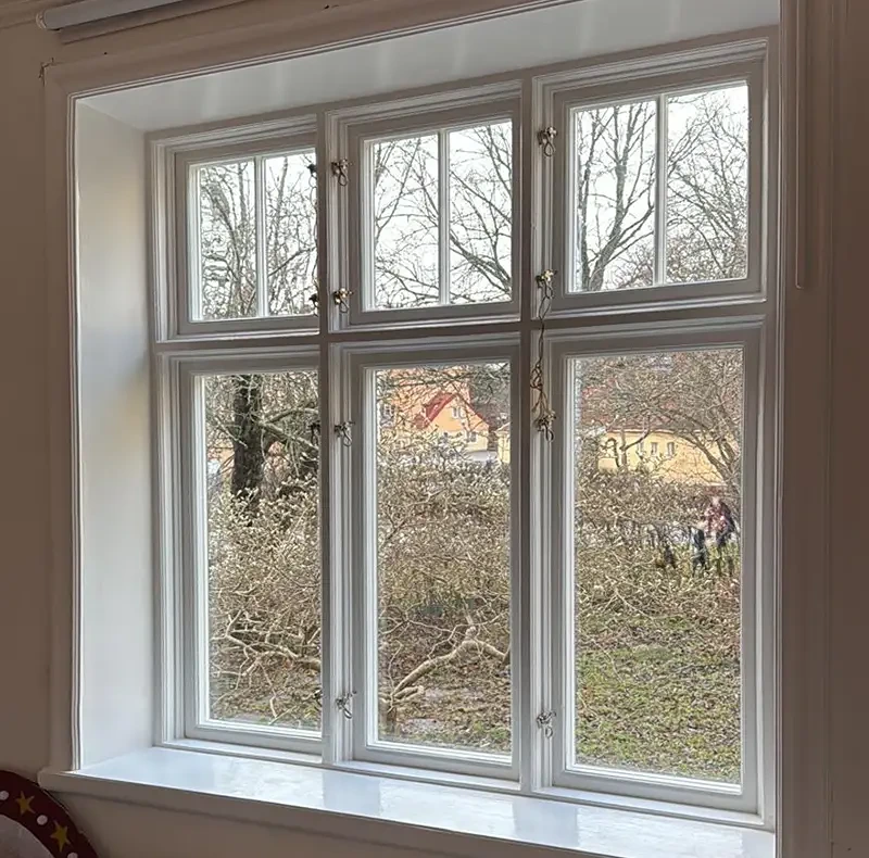 Vitt fönster med sexdelad spröjs och utsikt mot gård med hus.